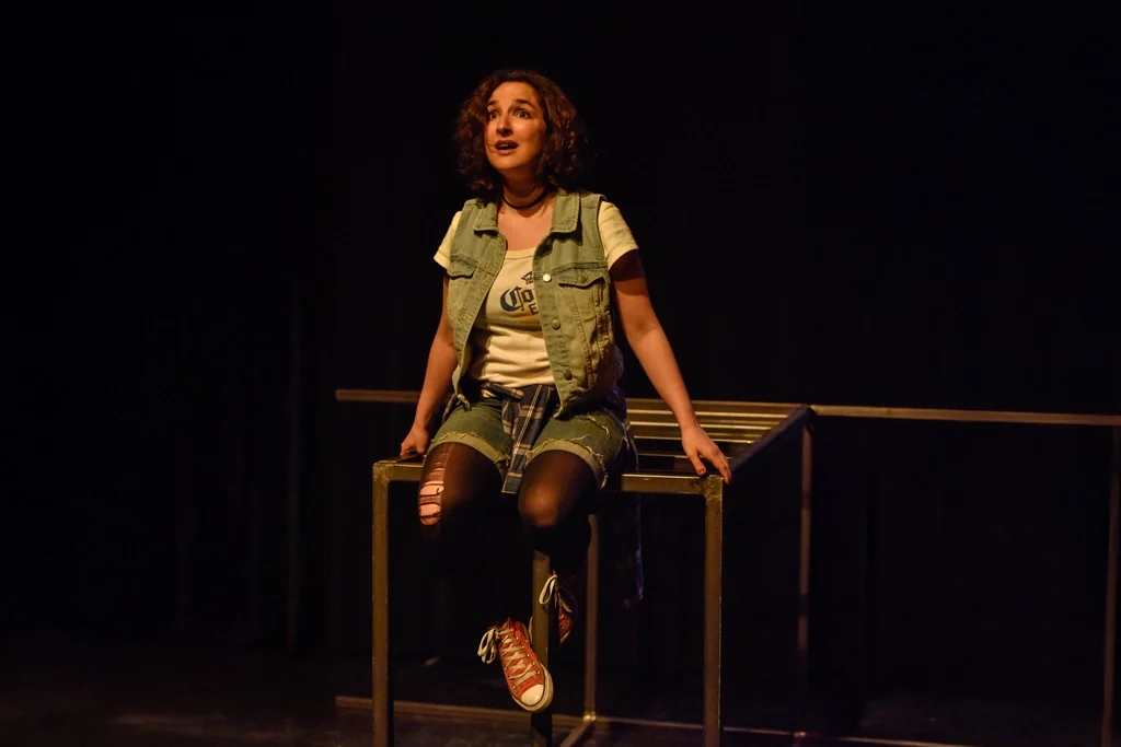 Actrice assise sur une structure métallique, exprimant une profonde réflexion.