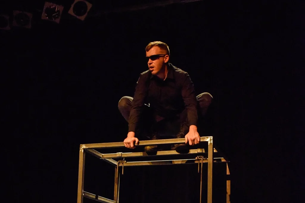 Acteur acrobate assis sur une structure métallique.